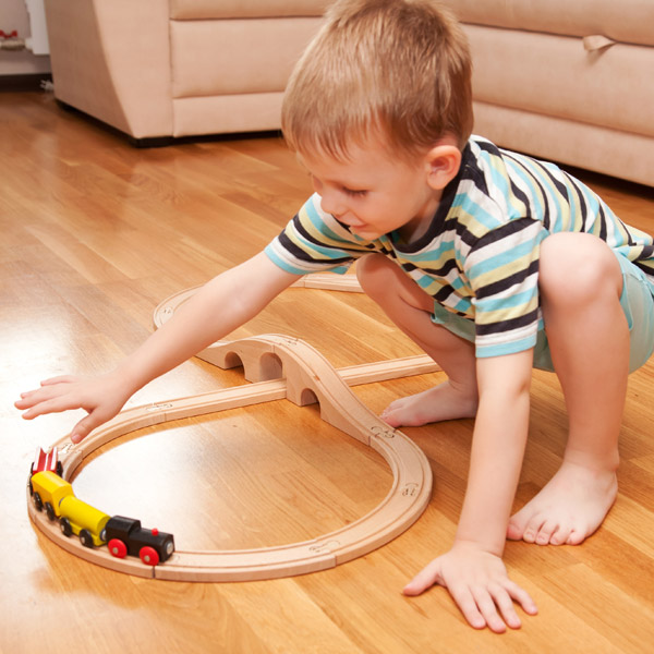 little kid playing with train set on clean wood floor